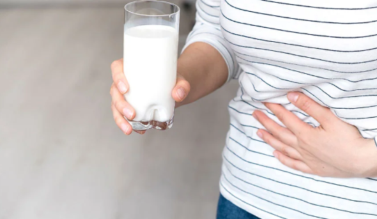 Frau mit einem Glas Milch in der Hand hält sich den Bauch - Laktoseintoleranz